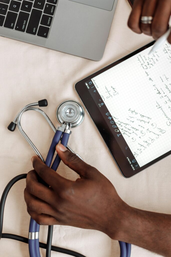 A close look at hands holding a stethoscope next to a tablet showing medical notes.